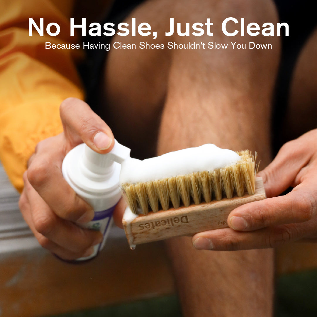Person holding a Delicates Brush and RTU Foam the two items included in the Quick Clean Kit with text 'No Hassle, Just Clean' on a blurred background.