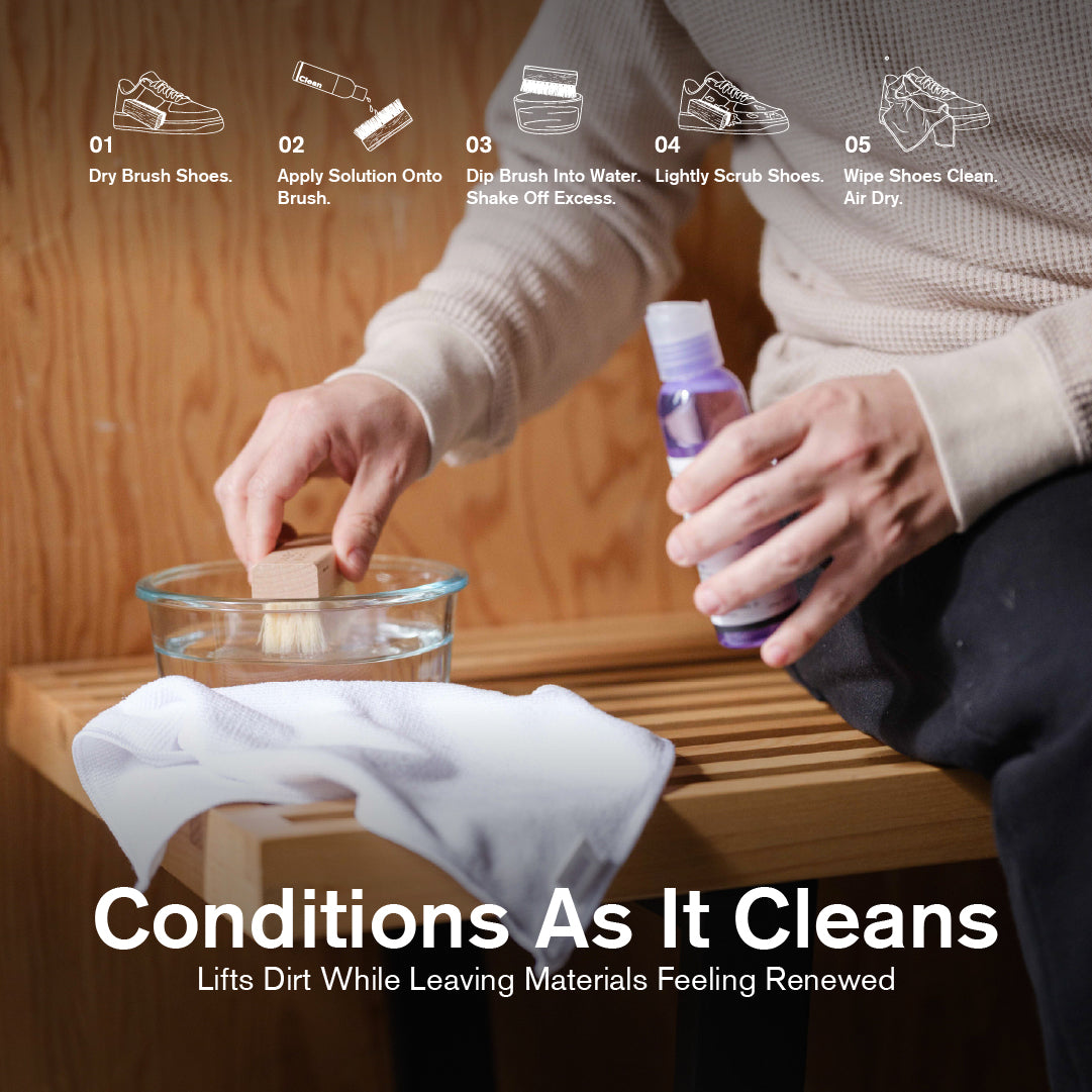 Person dipping a Jason Markk Durables wooden brush into a water bowl while holding Deep Cleaning Solution, with a white microfiber towel on a wood bench. Five-step guide shown: Dry Brush, Apply Solution, Dip in Water, Scrub Shoes, Wipe and Air Dry. Text reads: "Conditions As It Cleans – Lifts Dirt While Leaving Materials Feeling Renewed."