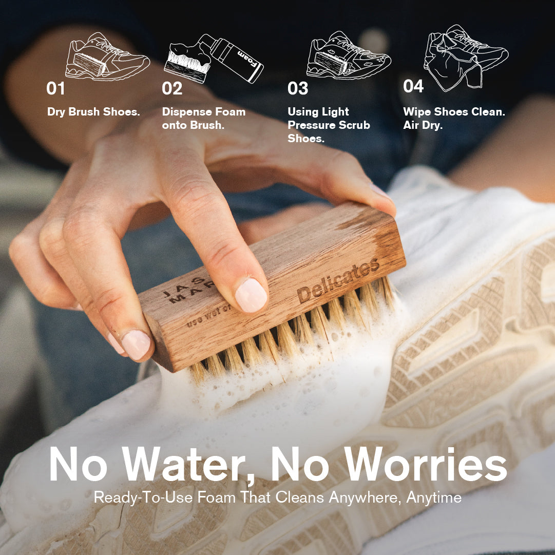 Hand using Jason Markk Delicates cleaning brush with foam on a white sneaker. Step icons and text read: “01 Dry Brush Shoes. 02 Dispense Foam onto Brush. 03 Using Light Pressure Scrub Shoes. 04 Wipe Shoes Clean. Air Dry.” Headline reads “No Water, No Worries” with subtext “Ready-To-Use Foam That Cleans Anywhere, Anytime.”