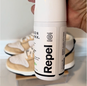 Repel spray bottle held by a hand with shoes in the background